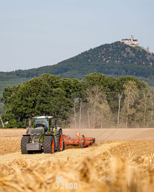 Traktor mit Bodenbearbeitungsgerät vor einer bewaldeten Hügellandschaft